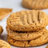 A stack of three peanut butter cookies with a crisscross fork pattern on top, surrounded by more cookies on a light surface.