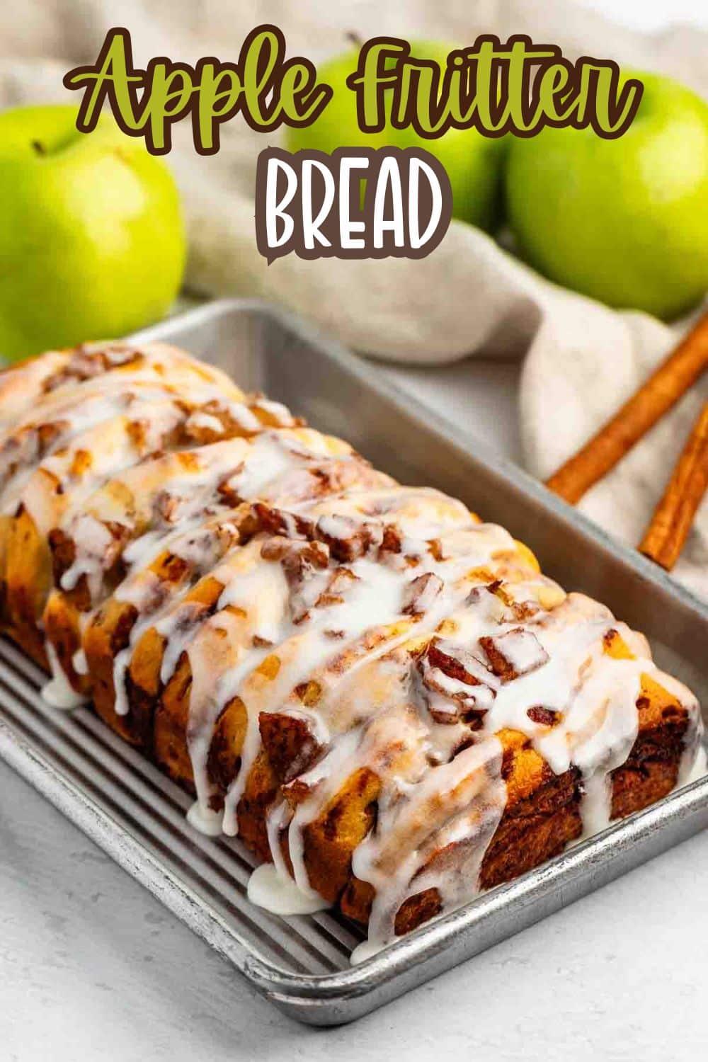 A loaf of apple fritter bread drizzled with white icing sits on a baking tray with two green apples, cinnamon sticks, and a beige cloth in the background. The text “Apple Fritter Bread” appears at the top.