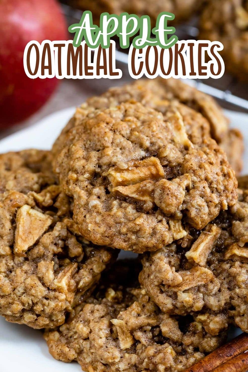 A close-up of apple oatmeal cookies stacked on a white plate, showcasing chunks of apple and oats. The text Apple Oatmeal Cookies is written above in a bold font. An apple and cinnamon sticks are in the background.