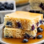 stacked square pancakes with blueberries baked in on a white plate covered in syrup.