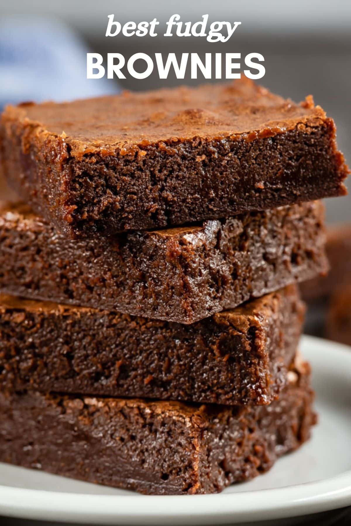 A close-up of four stacked, delectably fudgy brownies on a plate highlights their rich, chocolatey texture. The top brownie boasts a slightly crispy crust. Text at the top proclaims best fudgy BROWNIES.