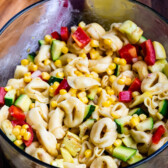 corn and zucchini and peppers and pasta and tomatoes all mixed together in a clear bowl