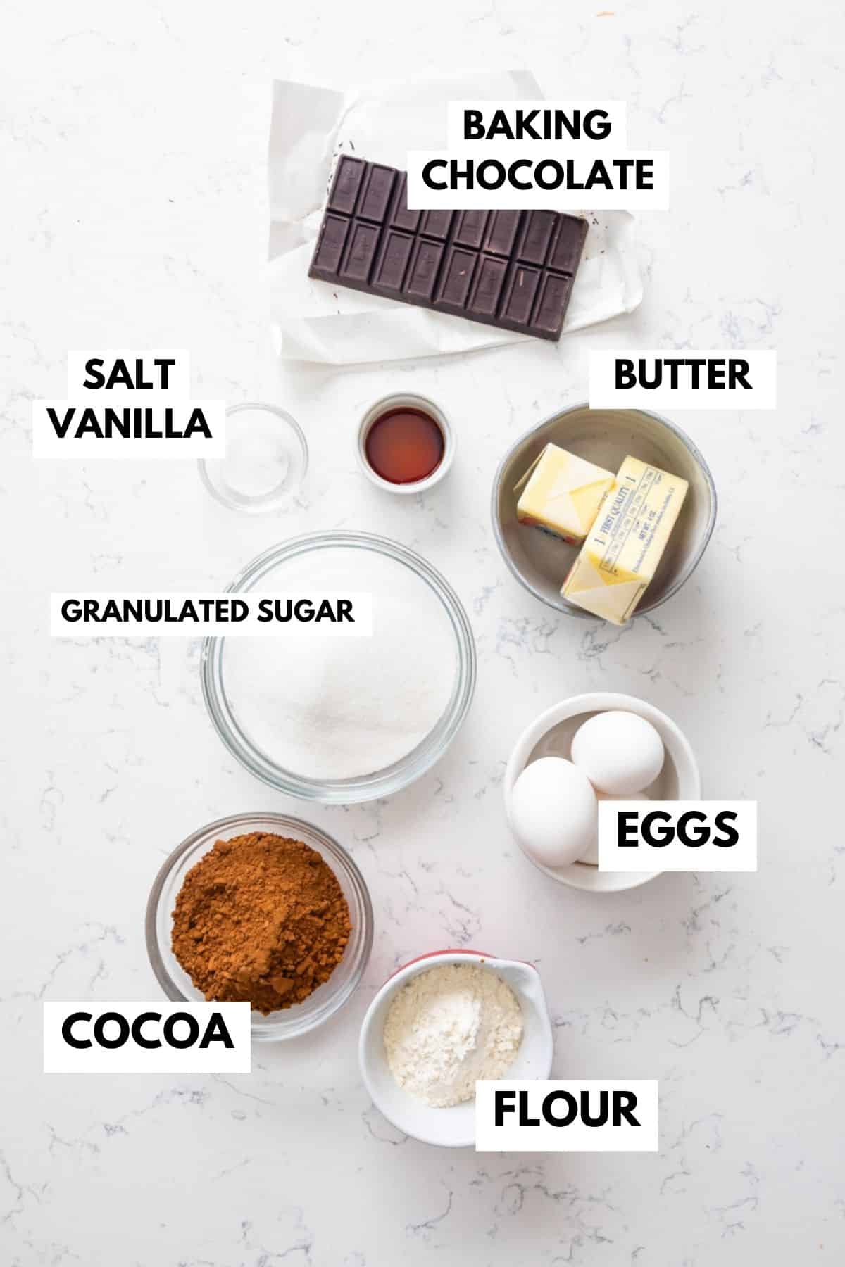 Ingredients for delectable brownies are spread out on a white surface: rich baking chocolate, creamy butter, fresh eggs, unsweetened cocoa, all-purpose flour, granulated sugar to sweeten the deal, a pinch of salt for balance, and aromatic vanilla.