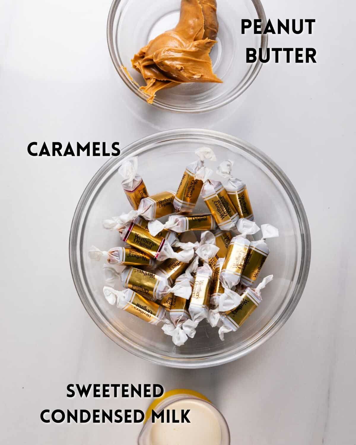 Three clear bowls on a white surface: one with caramels, one with peanut butter, and one with sweetened condensed milk. Each bowl is labeled with its contents in bold black text.