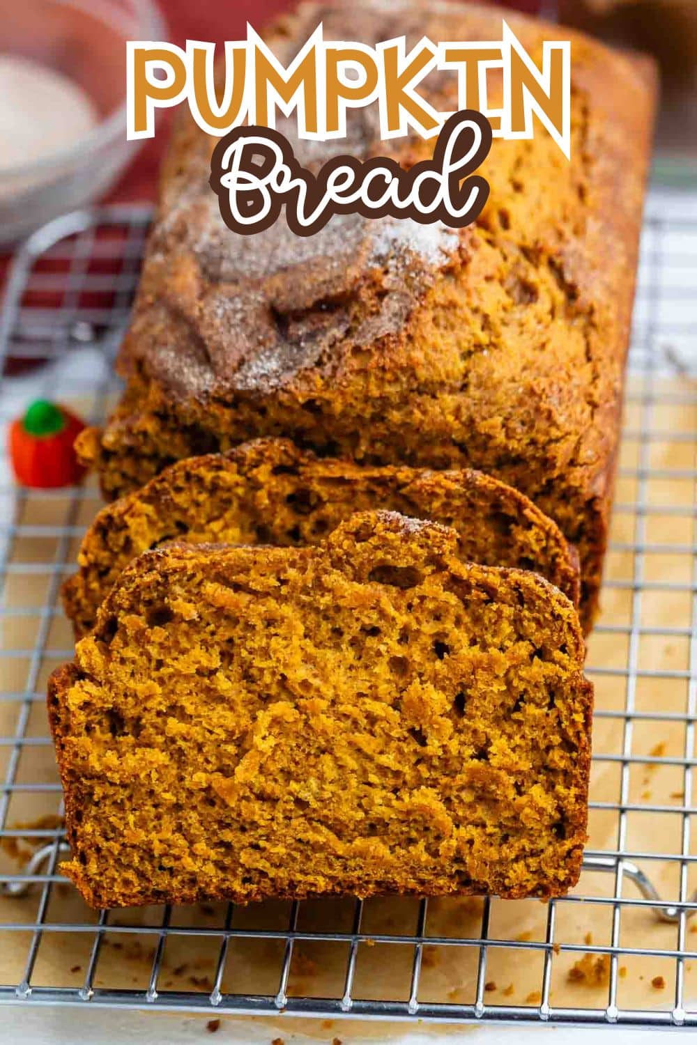 A loaf of pumpkin bread sits on a cooling rack, with three slices cut in front. The text Pumpkin Bread is written in bold letters at the top of the image.