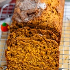A loaf of pumpkin bread is shown on a cooling rack, sliced to display its moist, orange interior