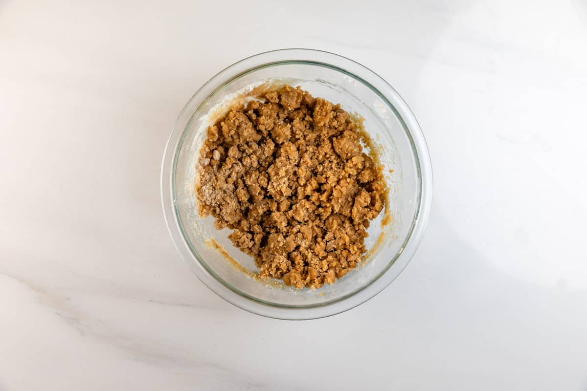 A glass bowl filled with a crumbly brown mixture sits on a white marble surface, viewed from above.