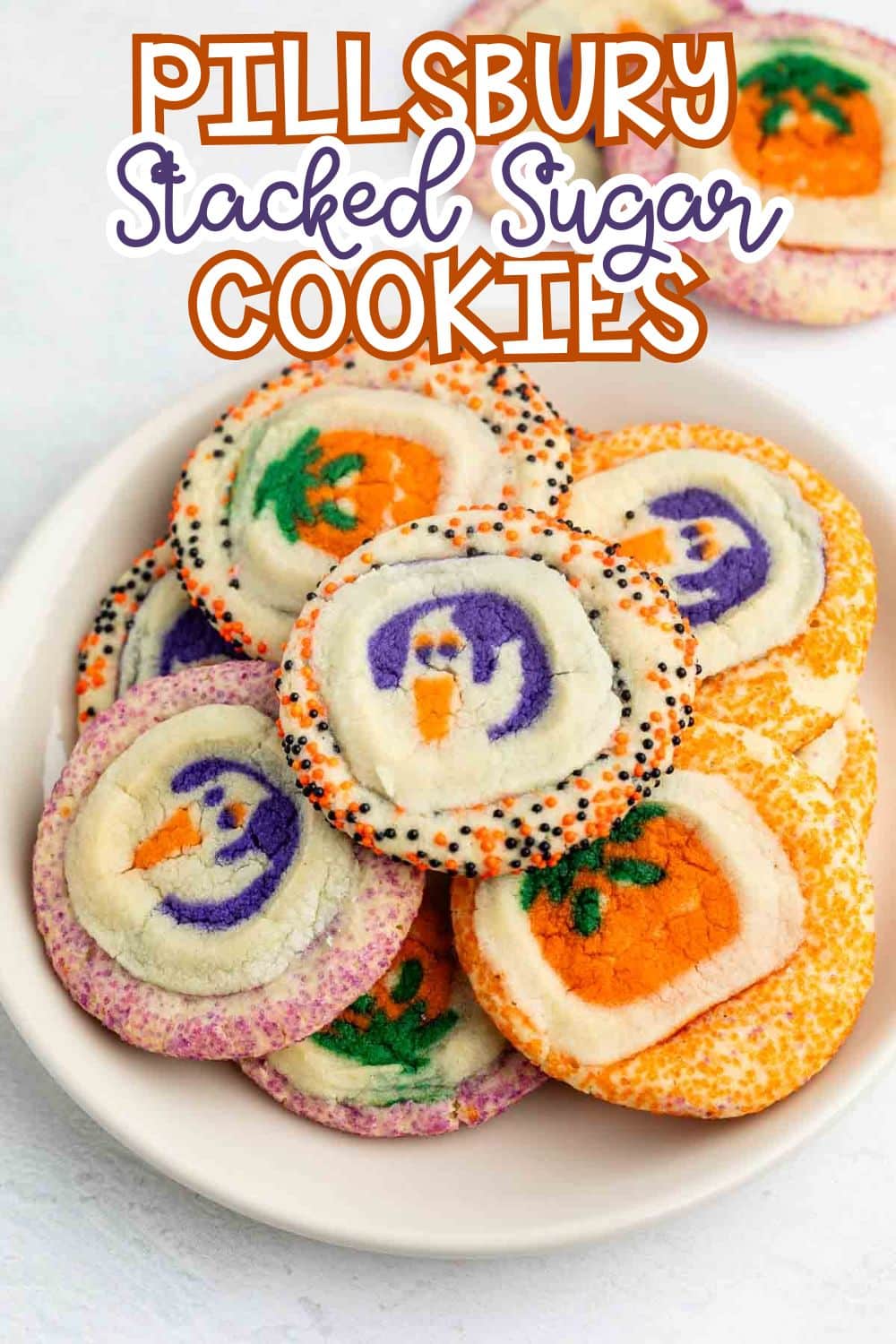 A plate of colorful Pillsbury stacked sugar cookies with Halloween-themed designs, including pumpkins and ghosts, surrounded by sprinkles. Text above reads Pillsbury Stacked Sugar Cookies.